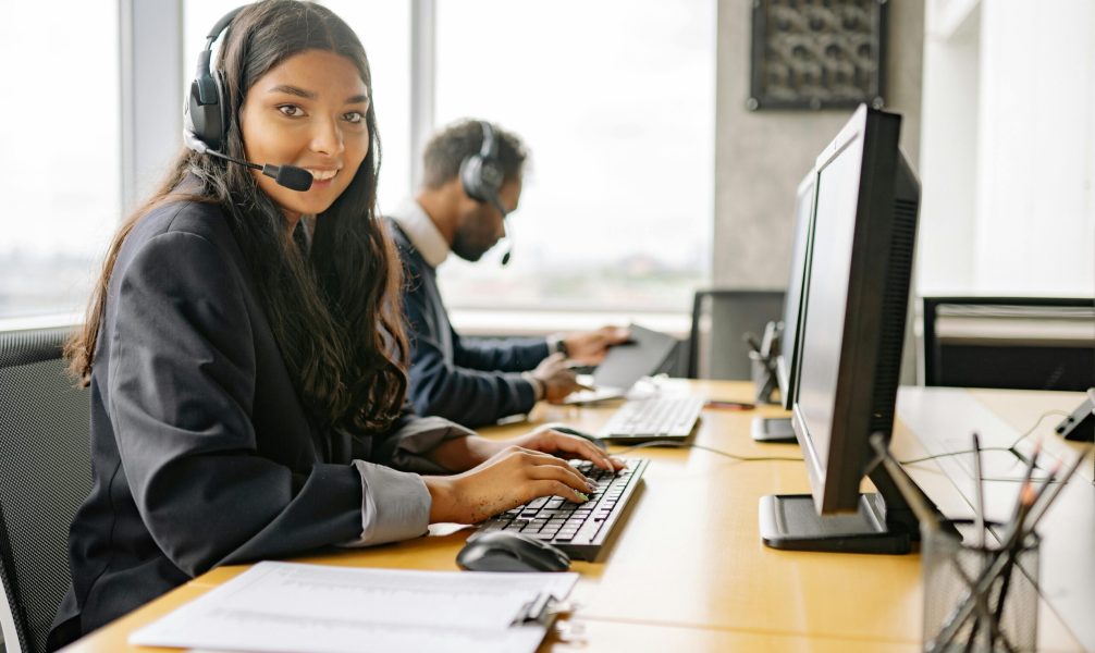 Smiling call center agents in an office providing customer support on computers.